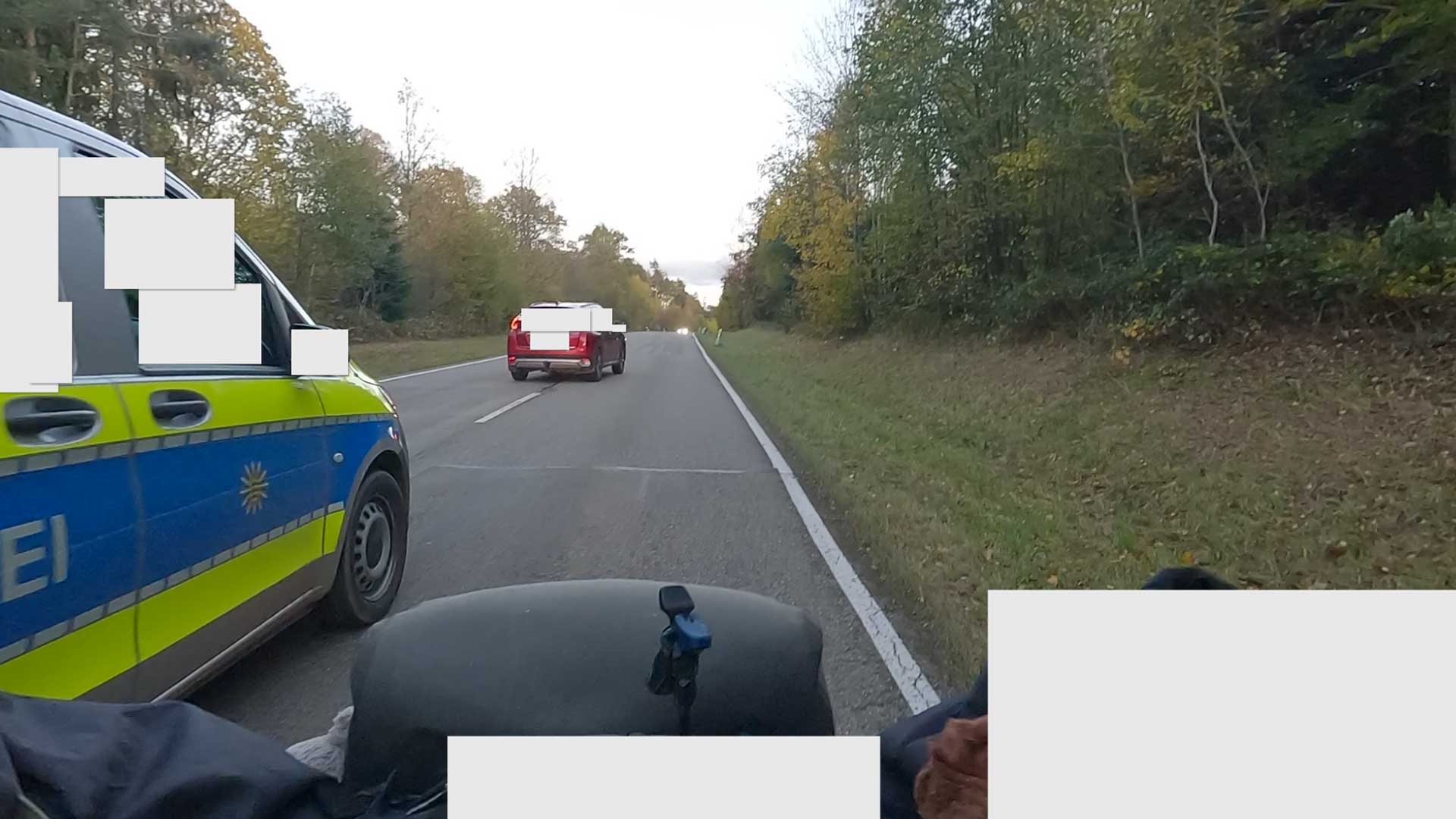 Foto einer Dash-Cam. Ein Rad-Fahrender wird von einem Polizei-Auto so eng überholt, dass das Fahrzeug den Rad-Fahrenden fast berührt.