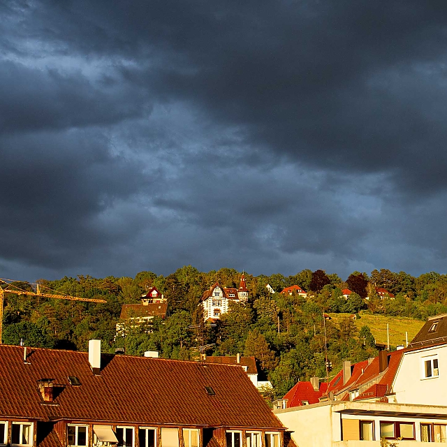 Kräftig dunkelblau-grauer Himmel (Kulisse) und golden angestrahlten Häusern (Vordergrund)