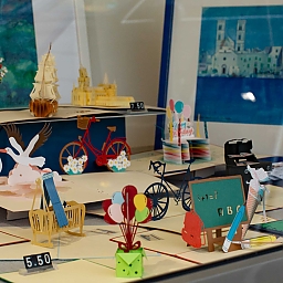 3D-Klappkarten von Artis Design mit unterschiedlichen Motiven: Kirschbäume, Fahrräder, Storch mit Baby zur Geburt, Luftballons, Schultafel, Segelboot, Mainzer Dom sowie einem Ölbild im Hintergrund.