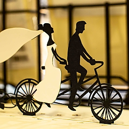 Foto einer 3D-Klappkarte mit einem radelnden Hochzeitspaar (sie mit wehendem Schleier auf dem hinteren Sattel) auf einem Tandem.