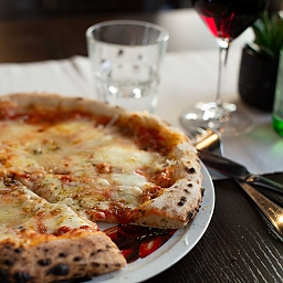 Nahaufnahme einer Pizza Quattro Formaggi. Im Hintergrund – unscharf, doch noch gut erkennbar – ein Glass Pellegrino und ein Glas Merlot.