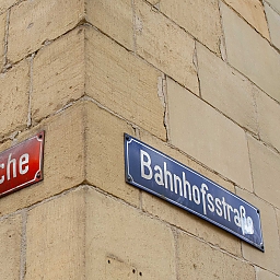 Straßenecke mit zwei Straßenschildern: links in Rot Hintere Bleiche (quer zum Rhein), rechts in Blau Bahnhofstraße (parallel zum Rhein)