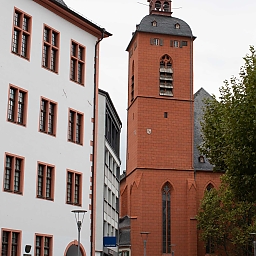 Altstadt von Mainz. Im Bild links Domus Universitatis (Alte Universität Mainz) mit geweißelten Mauern mit orange-rot umrandeten Fenstern. Die rechte Hälfte des Fotos zeigt die rote Backstein-Kirche St. Quintin.