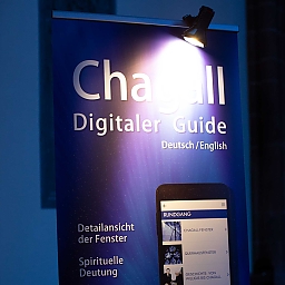 Info-Rollup zum Digitalen Guide für die Chagall-Kunst in St. Stephan mit Werbung für Detailansicht der Fenster, Spirituelle Deutung, Klais-Orgel und ihren Klang, Kreuzgang und die 1.000-jährige Geschichte