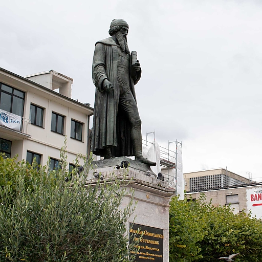 Denkmal für Gutenberg (stehend mit einem Buch in der linken Hand). Him Hintergrund ragt an einer Hauswand ein großes Transparent, das noch Werbung für die Ausstellung 