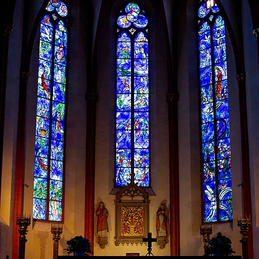 Gotische Rundbogen-Fenster mit Chagall-Motiven in kräftigem Kobalt-Blau, Rot, Occer, Grün mit Motiven aus der Bibel, die die freundlichen Beziehungen zwischen Christen und Juden symbolisieren (hinter dem Altar)