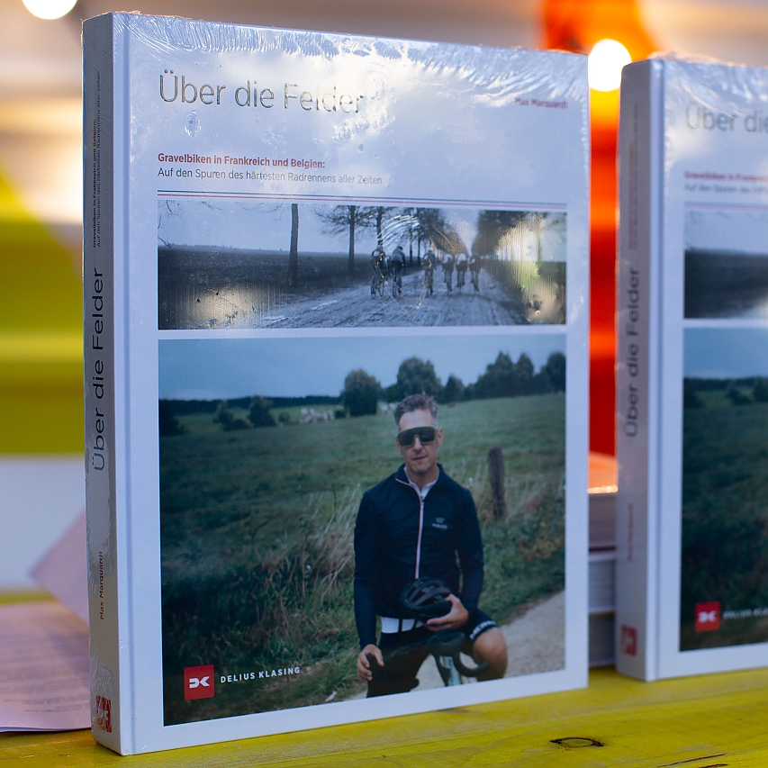 Leuchtend gelber Tisch. Darauf stehen zwei Ausgaben des Buches 