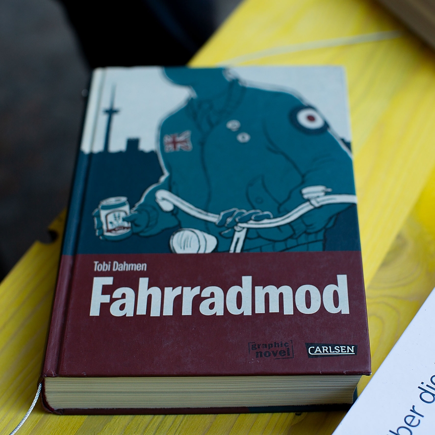 Knall-gelber Tisch. Darauf liegen verschiedene Bücher zum Thema Rad-Fahren. Im Fokus: Farradmod von Tobi Dahmen