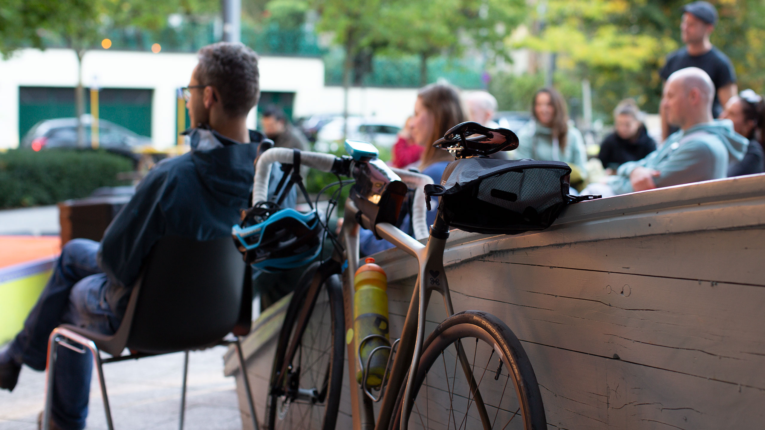 Szene vom RadFilmFest Stuttgart: Im Vordergrund scharf ein Rennrad (Männer) lehnt an einer Wand. Im Hintergrund unscharf die Zuhörenden einer Lesung.. Bild: cc FAHRRADkultur c/o Franziska Köppe | madiko