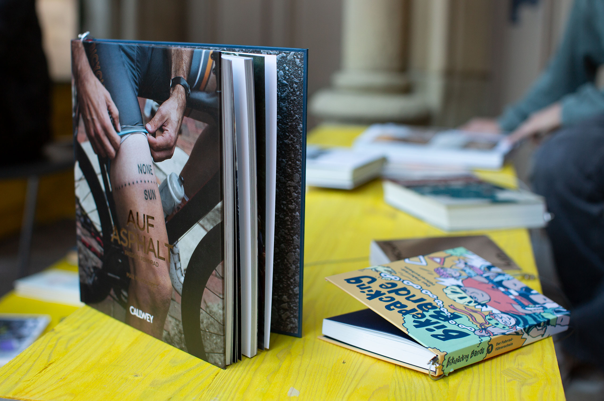Knall-gelber Tisch mit Büchern. Im Fokus steht das Buch Auf Asphalt von Max Marquardt.. Bild: cc FAHRRADkultur c/o Franziska Köppe | madiko